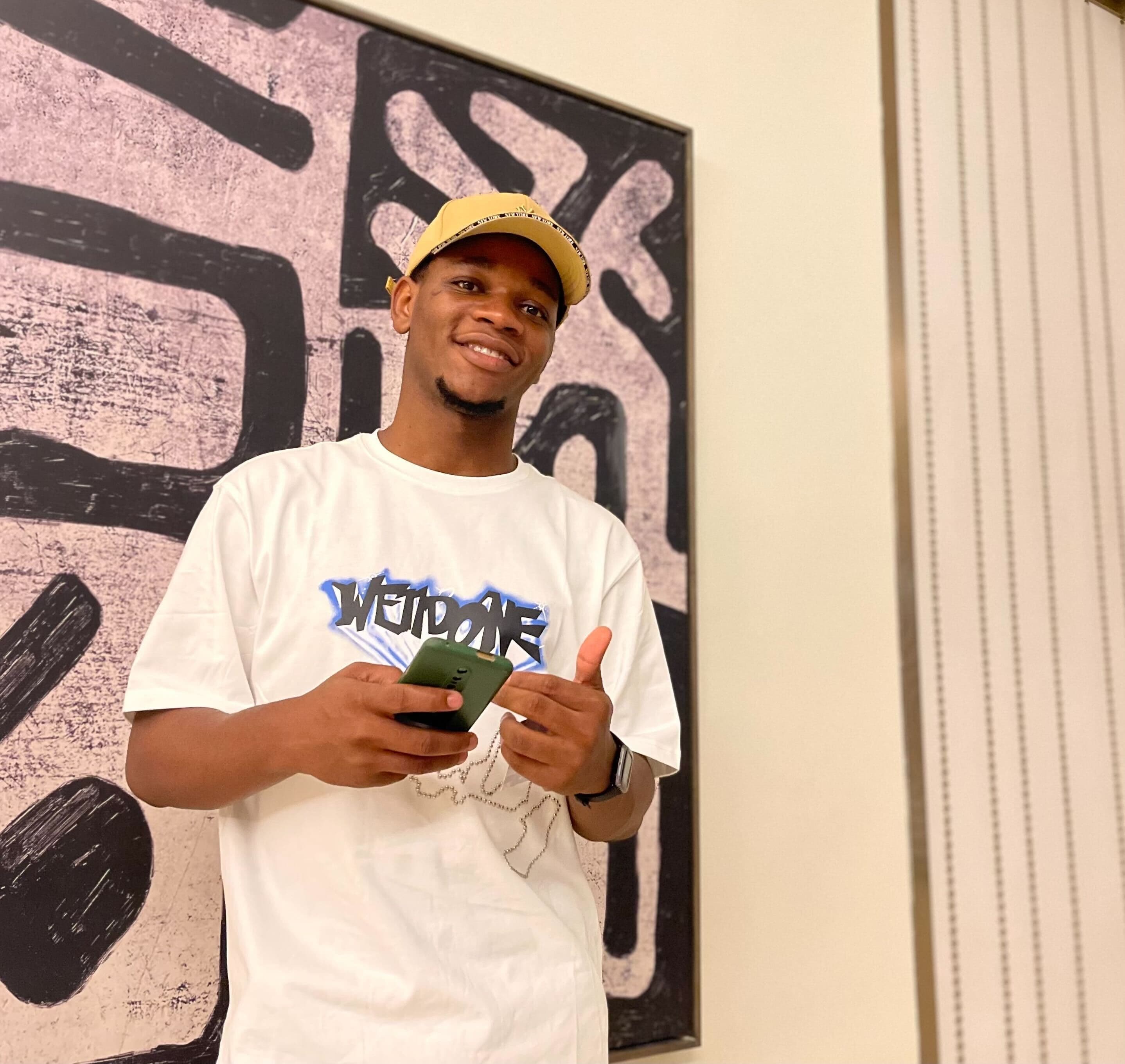 Kingsley Solomon, grinning with his phone in hand, in front of a graffiti canvas